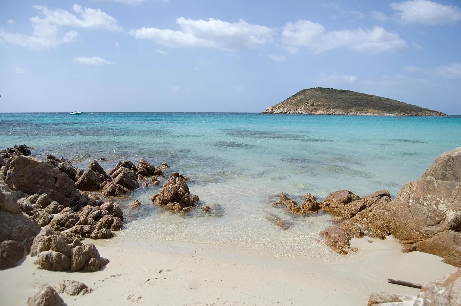 Spiaggia di Tuerredda con sabbia chiara e scogli in primo piano, mare turchese e trasparente e, al largo, l'isolotto coperto di macchia